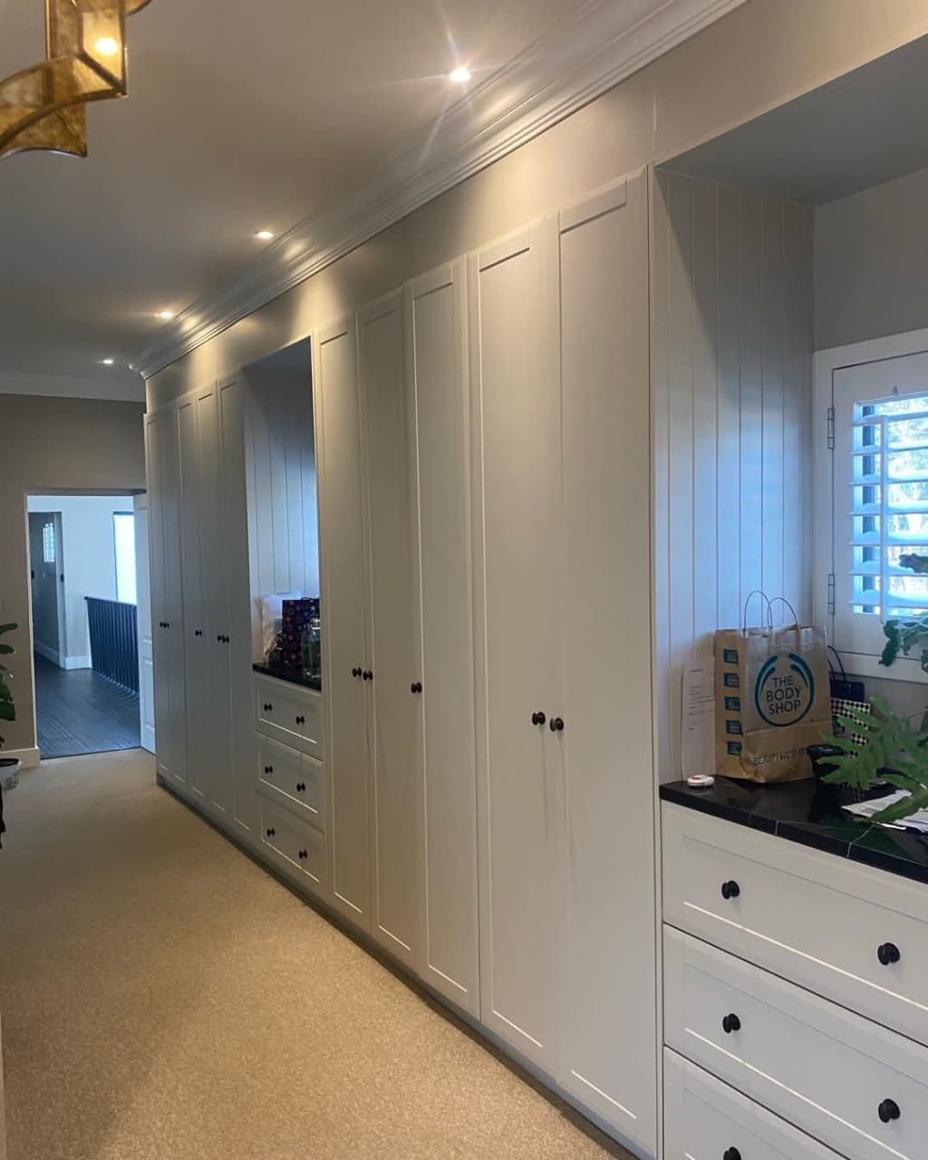 Floor-to-ceiling white built-in wardrobes with shaker doors along a hallway
