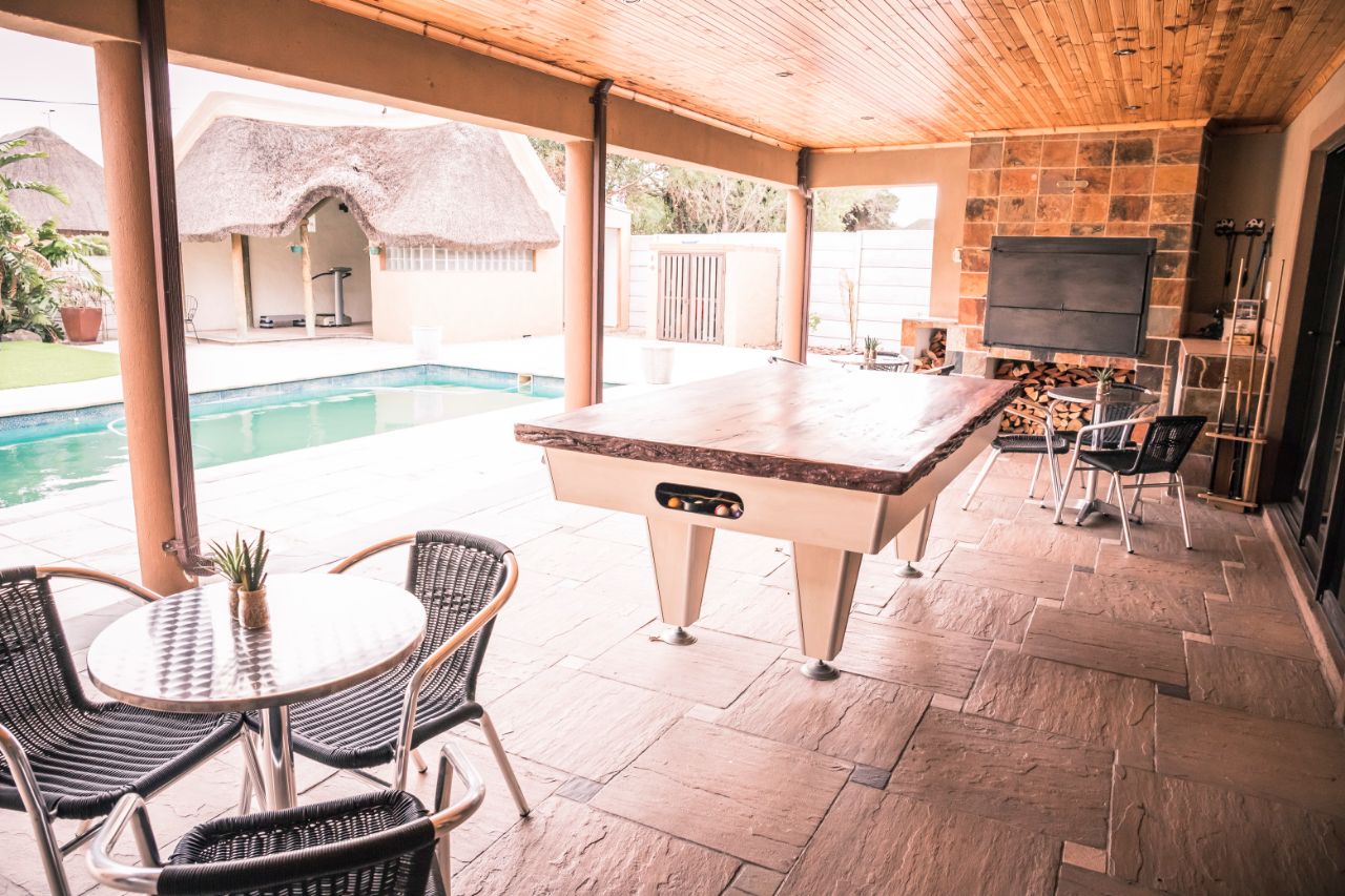 Outdoor covered patio with pool table, dining tables, braai fireplace and swimming pool at Therato Guest House