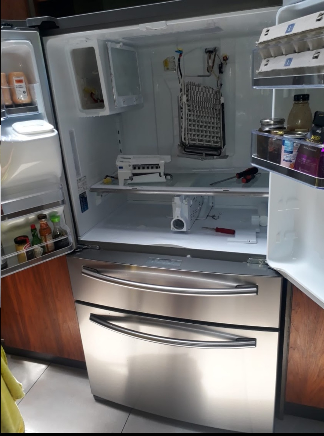 Open fridge freezer being repaired, with the ice maker and fan exposed