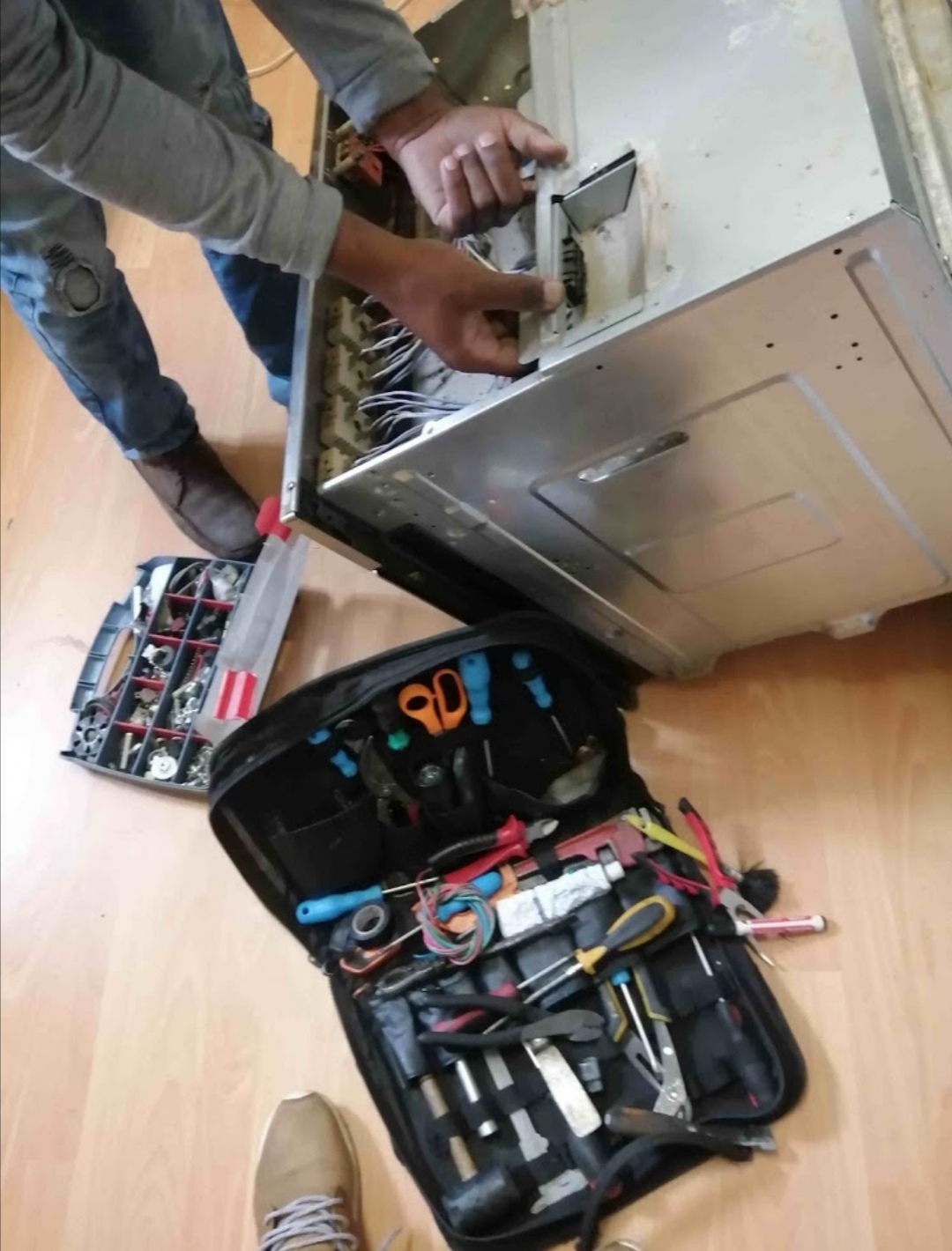 Technician working inside a stainless steel appliance with a full toolkit on the floor