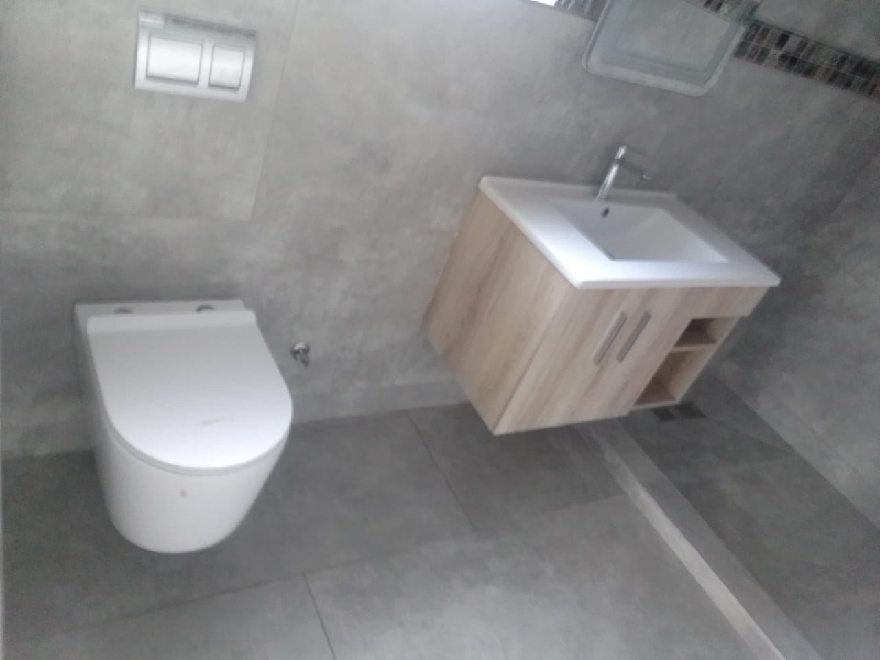 Modern grey-tiled bathroom with a wall-hung toilet and floating wood-effect vanity