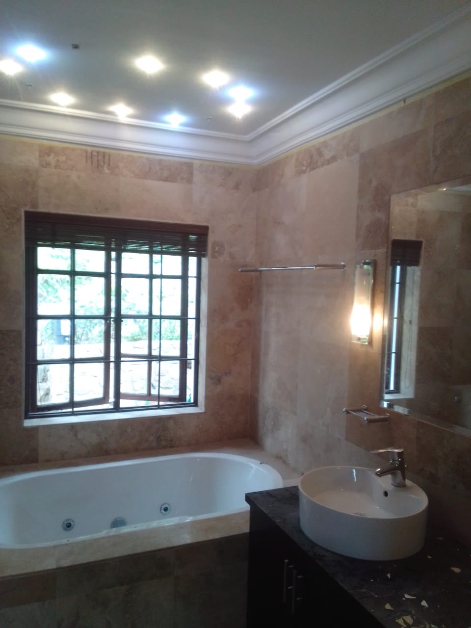 Bathroom with travertine-tiled walls, a jacuzzi bath, downlights and a vessel basin