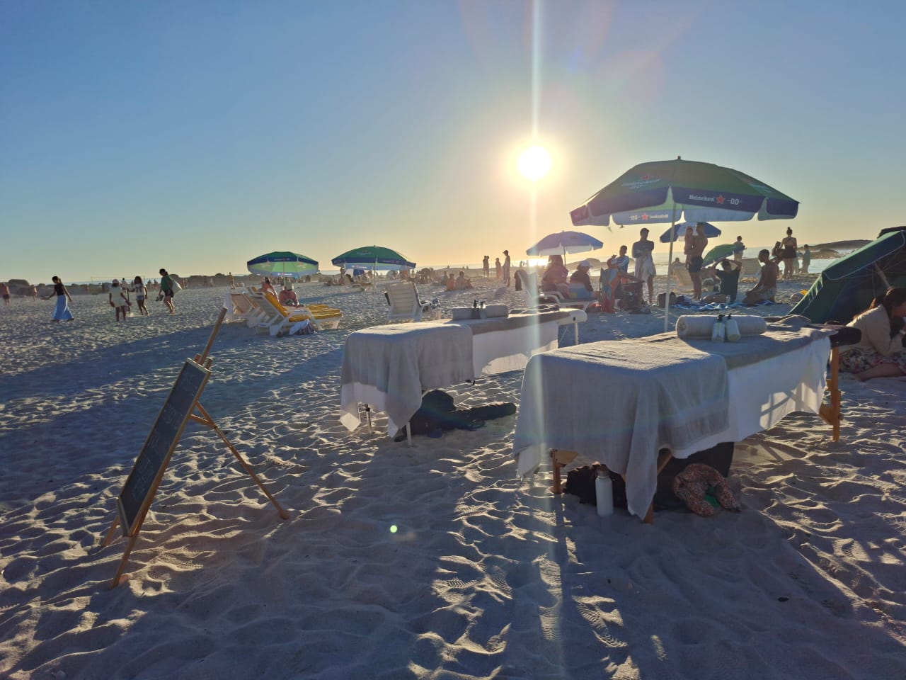 Outdoor beach massage setup on the white sands of Camps Bay beach at golden hour sunset