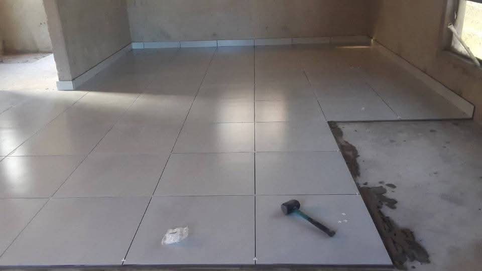 Grey floor tiles being laid square across an unfinished room