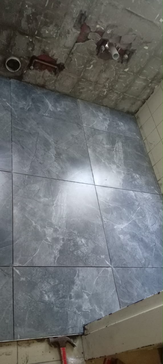Grey marble-effect floor tiles being installed beside a plastered wall