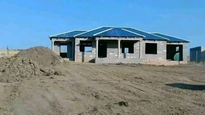 Block house with a blue roof under construction on cleared land, by Mundende Building Construction and Carpentry