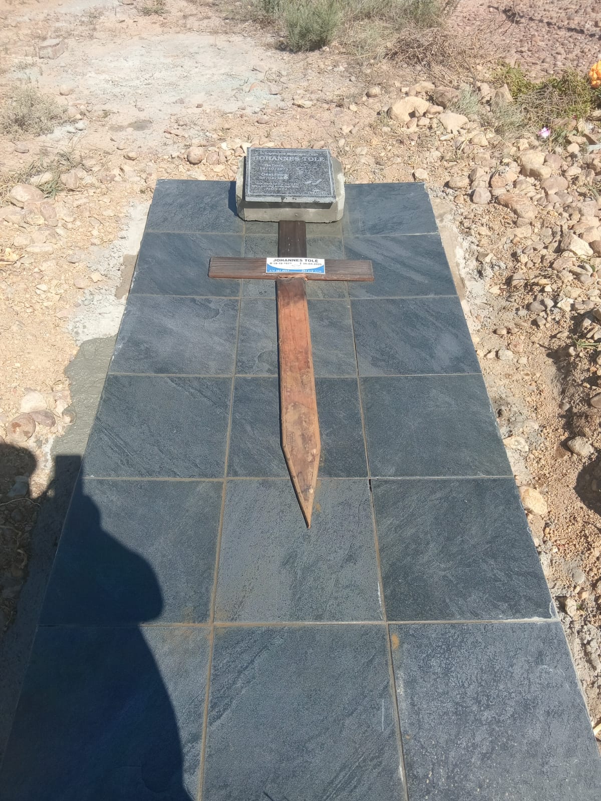 A finished grave with dark slate tiles, a wooden cross and a name plaque.