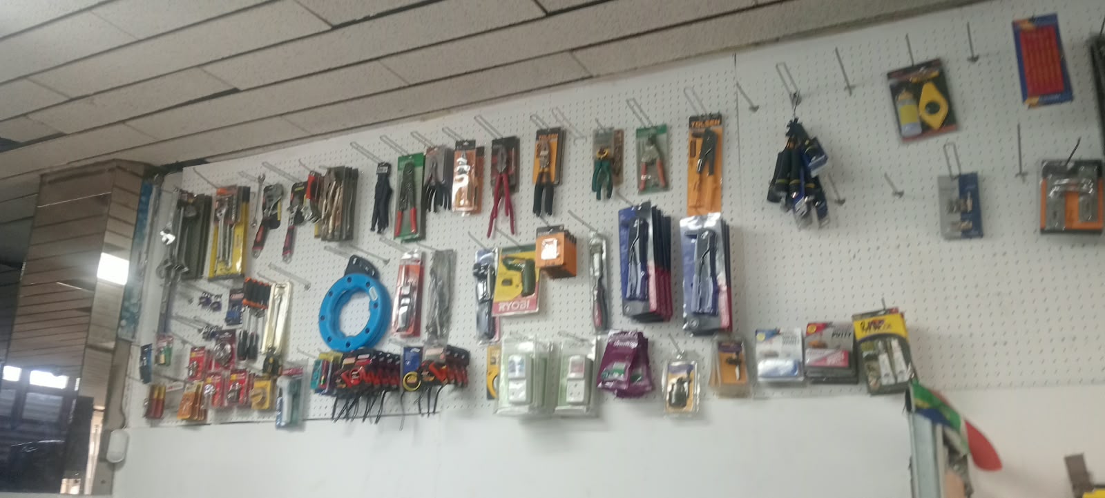 Pegboard wall of hand tools with pliers, spanners, screwdrivers, a blue cable reel and a Ryobi tool